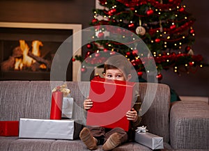 Little boy hiding behind gift box at christmas