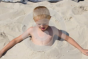 Little boy hiding himself in sand on the beach