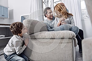 Little boy hiding while his parents hugging and talking