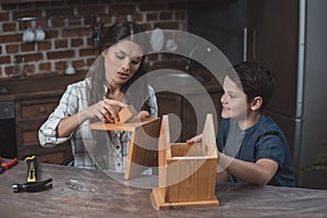 Little boy and his beautiful mother crafting a wooden birdhouse at home