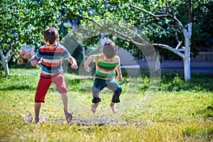 Little boy and his brother play in summer park. Children with colorful clothes jump in puddle and mud in the garden.