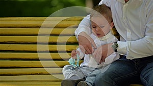 Little boy and his dad does not want to try on a bow tie. They are sitting on a park bench.