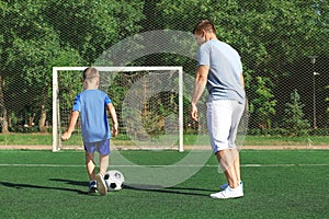 Little boy with his dad playing football on soccer pitch