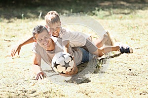 Little boy and his dad with soccer ball lying on grass outdoors