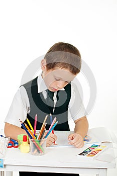 Little boy at his desk with an album for drawing, pencils and books on white background