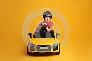 Little boy with his dog in toy car on yellow background