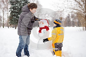 Little boy with his father building snowman in snowy park. Active outdoors leisure with children in winter