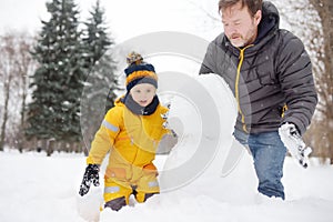 Little boy with his father building snowman in snowy park. Active outdoors leisure with children in winter