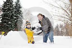 Little boy with his father building snowman in snowy park. Active outdoors leisure with children in winter