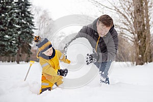 Little boy with his father building snowman in snowy park. Active outdoors leisure with children in winter