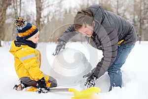 Little boy with his father building snowman in snowy park. Active outdoors leisure with children in winter