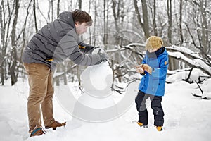 Little boy with his father building snowman in snowy park. Active outdoors leisure with children in winter. Kid during stroll in a