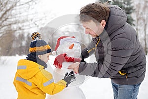 Little boy with his father building snowman in snowy park. Active outdoors leisure with children in winter