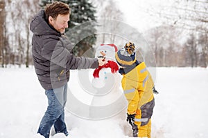 Little boy with his father building snowman in snowy park. Active outdoors leisure with children in winter