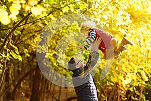 Little boy and his father having fun during stroll in the forest on sunny autumn day. Dad throws child up. Hiking with little kids