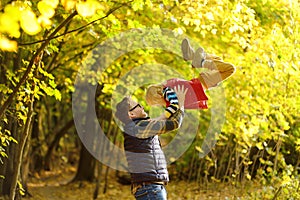 Little boy and his father having fun during stroll in the forest on sunny autumn day. Dad throws child up. Quality family time