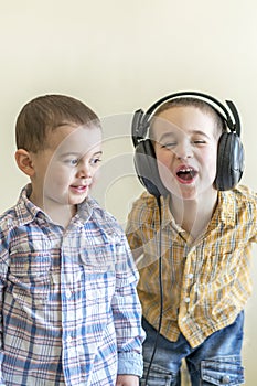 A little boy with his headphones dances with his brother. Two little brothers in shirts amuse themselves and dance.