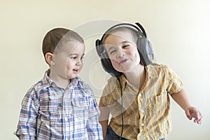 A little boy with his headphones dances with his brother. Two little brothers in shirts amuse themselves and dance.