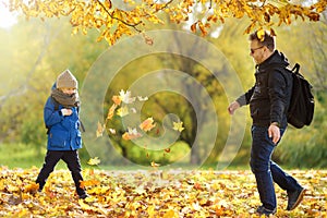 Little boy and his mature father having fun during stroll in the city park at sunny cold autumn day. Child and dad playing maple