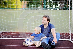 Little boy and his middle age father having fun playing a soccer/football game on summer day