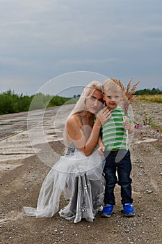 A little boy with his mom`s blonde standing in  field on the runway