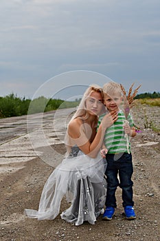 A little boy with his mom`s blonde standing in  field on the runway