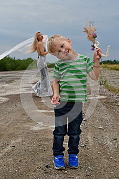 A little boy with his mom`s blonde standing in  field on the runway