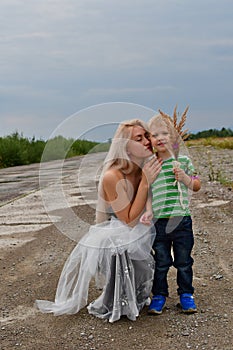 A little boy with his mom`s blonde standing in  field on the runway