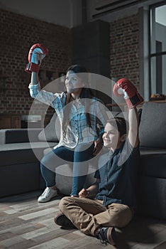 Little boy and his mother cheering while wearing boxing gloves and watching match