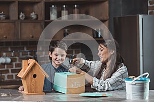 Little boy and his mother sitting at home and building wooden birdhouses