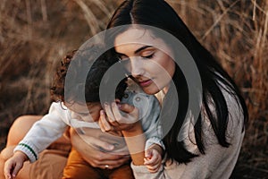 Little boy and his mother walking in the autumn park. Mother hugs her toddler boy