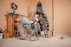 Little boy and his old grandfather on a wheelchair sitting near Christmas tree