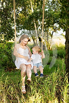 A little boy with his pregnant mother sitting on a swing.