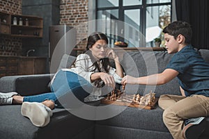 Little boy and his young mother playing chess on couch