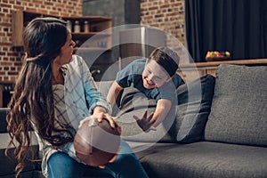 Little boy and his young mother playing with a rugby ball on couch