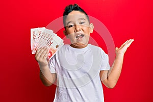 Little boy hispanic kid holding 20 israel shekels banknotes celebrating achievement with happy smile and winner expression with