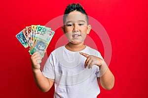 Little boy hispanic kid holding australian dollars smiling happy pointing with hand and finger