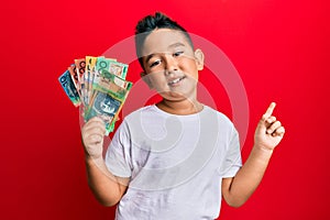 Little boy hispanic kid holding australian dollars smiling happy pointing with hand and finger to the side