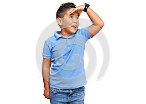 Little boy hispanic kid wearing casual clothes very happy and smiling looking far away with hand over head