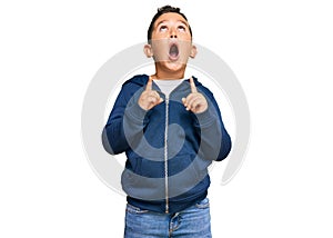 Little boy hispanic kid wearing casual sporty jacket amazed and surprised looking up and pointing with fingers and raised arms