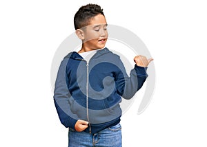 Little boy hispanic kid wearing casual sporty jacket smiling with happy face looking and pointing to the side with thumb up