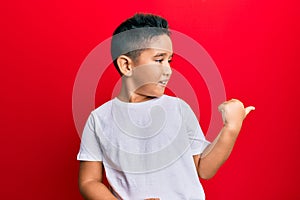 Little boy hispanic kid wearing casual white tshirt smiling with happy face looking and pointing to the side with thumb up
