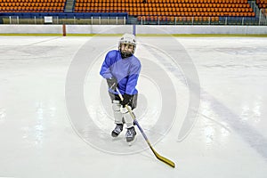 Little boy hockey player in blaue uniform posing with a hockey stick on ice hockey rink. Sport for children