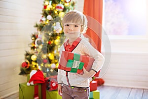 Little boy hold a gift box near a decorated Christmas tree