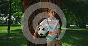 Little boy hold soccerball lean on tree. Young athlete posing with ball closeup.