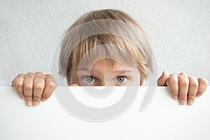 Little boy holding blank white sign or placard hiding his face