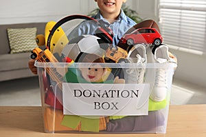 Little boy holding donation box with goods and toys at home, closeup