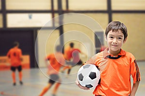 Little boy holding football in futsal gym