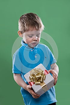 A little boy holding a gift box in his hands isolated on the green background