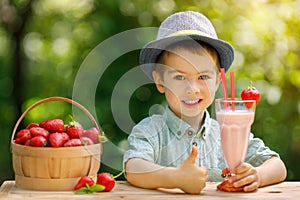 little boy holding glass of strawberry milkshake outdoors